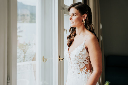 Bride gazing out window before lakeside wedding