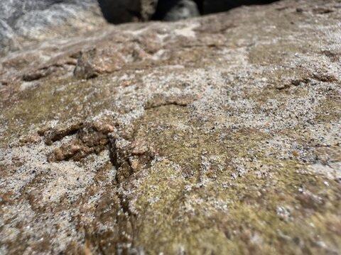 A close-up view of wind-blown sand settled among the rocks of a riprap coastal border at Carlsbad State Beach.