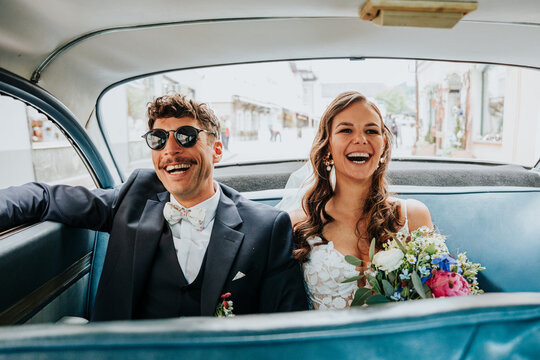 Bride and groom laughing together in wedding car