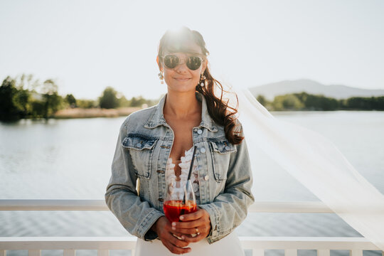 Bride in denim jacket holding cocktail during relaxed wedding ce