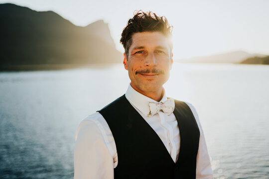 Relaxed professional man standing outdoors near lake at sunset