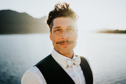 Confident man in formal vest smiling at sunset by lake