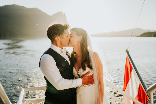 Bride and groom kissing on boat during golden hour lake wedding