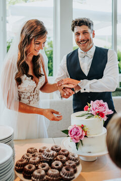 Bride and groom laughing while cutting cake at wedding reception