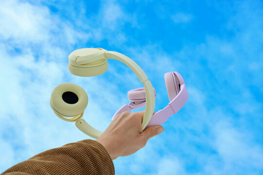 Hand holding headphones against blue sky