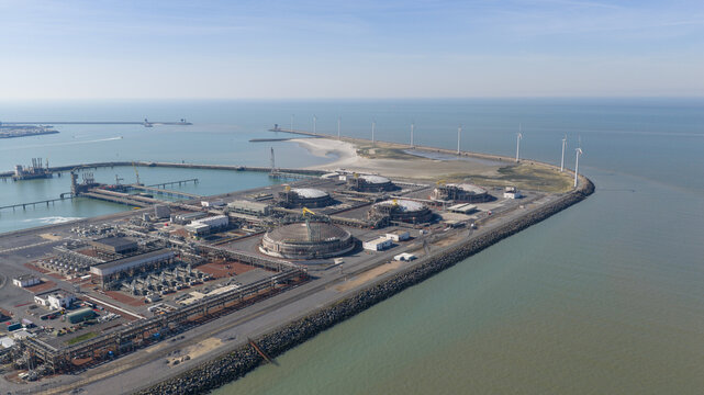 Aerial view of the Fluxys LNG Terminal Zeebrugge with its massive storage tanks and a row of wind turbines along the breakwater in Brugge, Vlaanderen, Belgium.