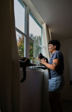 woman happily petting cat in window perch 