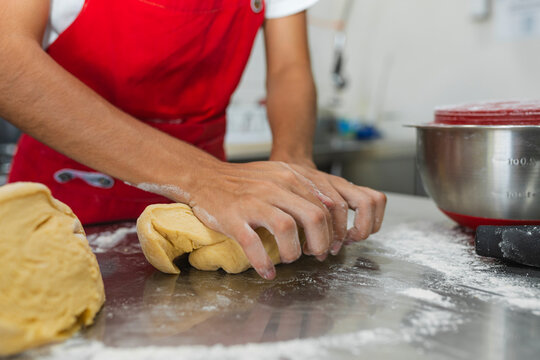 Chef hands kneading bread dough on metal table
