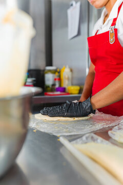 Chef with black gloves flattening dough on plastic for empanadas