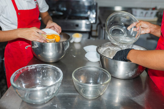 Cooks adding eggs and water to mixing bowl