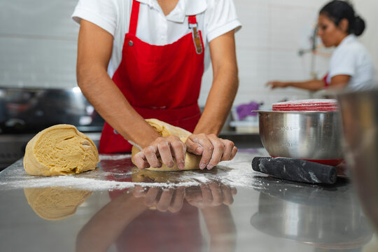 Female chef kneading a portion of dough on a shiny metal table