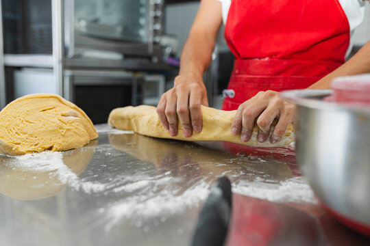Female chef stretching a portion of dough on a shiny metal table
