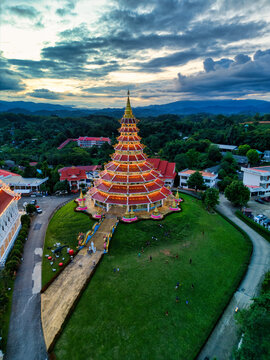 Aerial view of the illuminated Wat Huay Pla Kang pagoda with its multi-tiered roof surrounded by green lawns and rolling hills at dusk in Tambon Ban Du, Chang Wat Chiang Rai, Thailand.