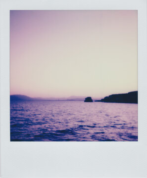 Polaroid landscape of a calm sea and distant rock formation at twiligh