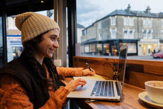 Woman wearing a beanie working on laptop in London cafe