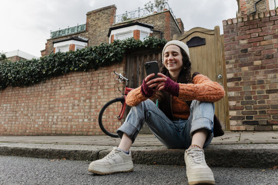Woman sitting sidewalk using smartphone happy messaging