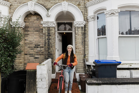Woman leaving brick house with bicycle for daily commute