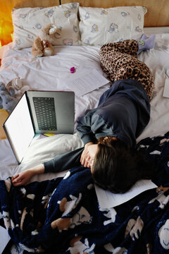 Person sleeping overwhelmed on bed near laptop