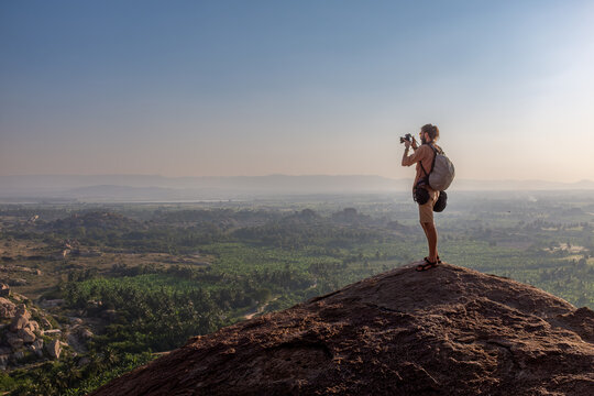 Travel photographer standing on rock overlooking Hampi landscape