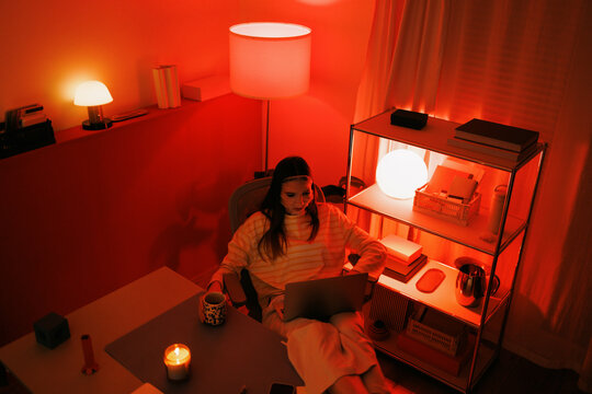 Woman enjoying beauty and skincare tips on laptop in red-lit home