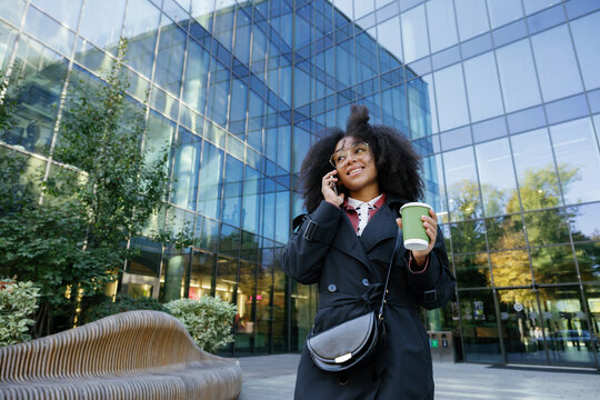 Bottom view of smiling black woman with coffee calling on smartphone