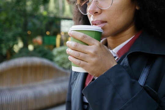 Obscure face of cropped black businesswoman drinking coffee from cup