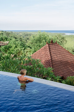 Woman relaxing in infinity pool overlooking tropical coastline