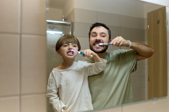 Father and son brushing teeth together in bathroom