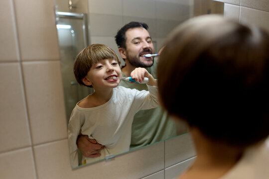 Father and son brushing teeth together in bathroom
