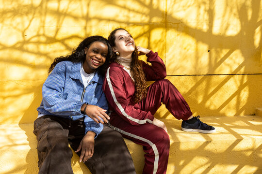 Two GenZ friends laughing over yellow building on the street