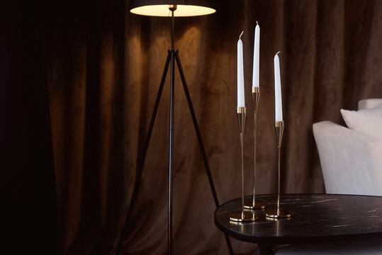Candles on a table beside a lamp in a living room with brown curtains