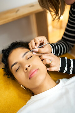 Woman receiving eyebrow plucking treatment in beauty salon
