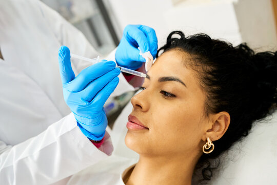 Woman receiving cosmetic injection on forehead in beauty salon