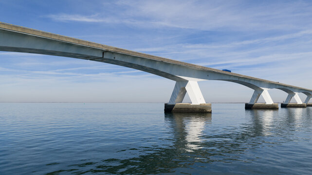 Aerial view of Zeeland Bridge spanning across calm blue water under a clear sky with soft clouds in Zierikzee, Zeeland, Netherlands.