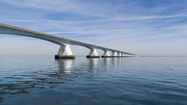 Aerial view of the Zeeland Bridge stretching across the calm Oosterschelde water under a blue sky in Zierikzee, Zeeland, Netherlands.