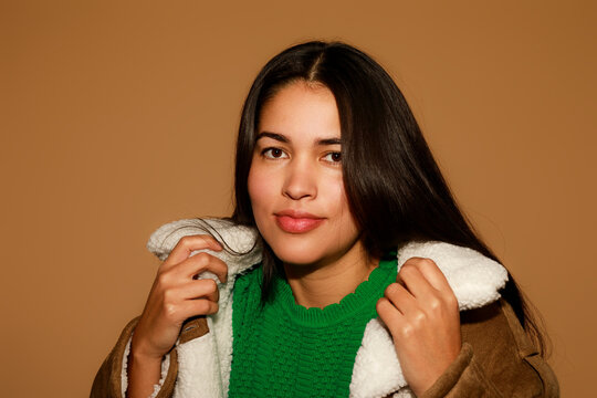 Woman Poses in a Cozy Sweater and Jacket Against a Plain Backdrop