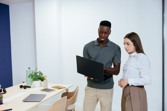 Diverse colleagues collaborating using laptop in modern office