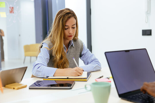 Professional woman writing notes during team meeting
