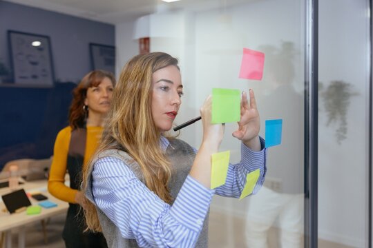 Businesswomen collaborating on ideas using sticky notes on glass wall