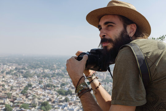 Bearded traveler holding camera at scenic viewpoint overlooking city