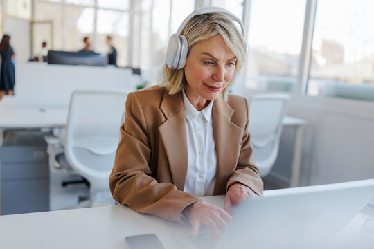 Business professional with headphones typing on laptop in office