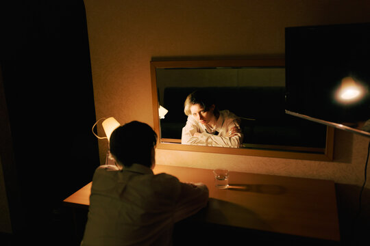 Person Sits at a Desk Looking at Reflection in a Mirror