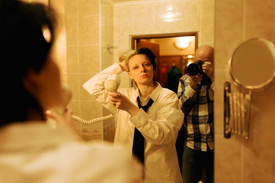 Person Uses Hair Dryer in Bathroom While Another Person Takes Photo