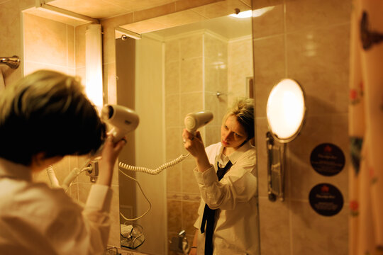 Woman Drying Her Hair in a Bathroom Mirror at Night