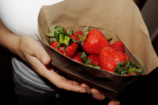 woman holds a paper bag with strawberries