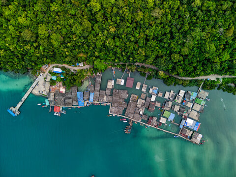 Aerial view of a traditional fishing village with wooden houses on stilts along the turquoise coastline and dense tropical forest in Ko Kut District, Trat, Thailand.