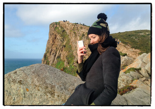 Woman using smartphone on cliffs at Cabo da Roca Portugal
