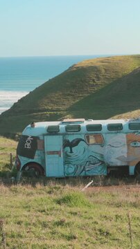 RAGLAN, NEW ZEALAND, 7 April 2026 &ndash; An abandoned, graffiti-covered bus sits on a grassy hillside overlooking the ocean, a symbol of forgotten journeys and artistic expression.