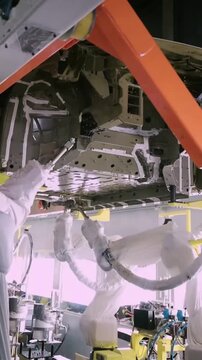 Vertical close up of industrial robots wearing white protective suits precisely assembling the underbody of a vehicle on a modern Chinese automotive production line