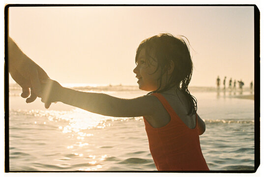 Child holding parent hand in ocean at sunset